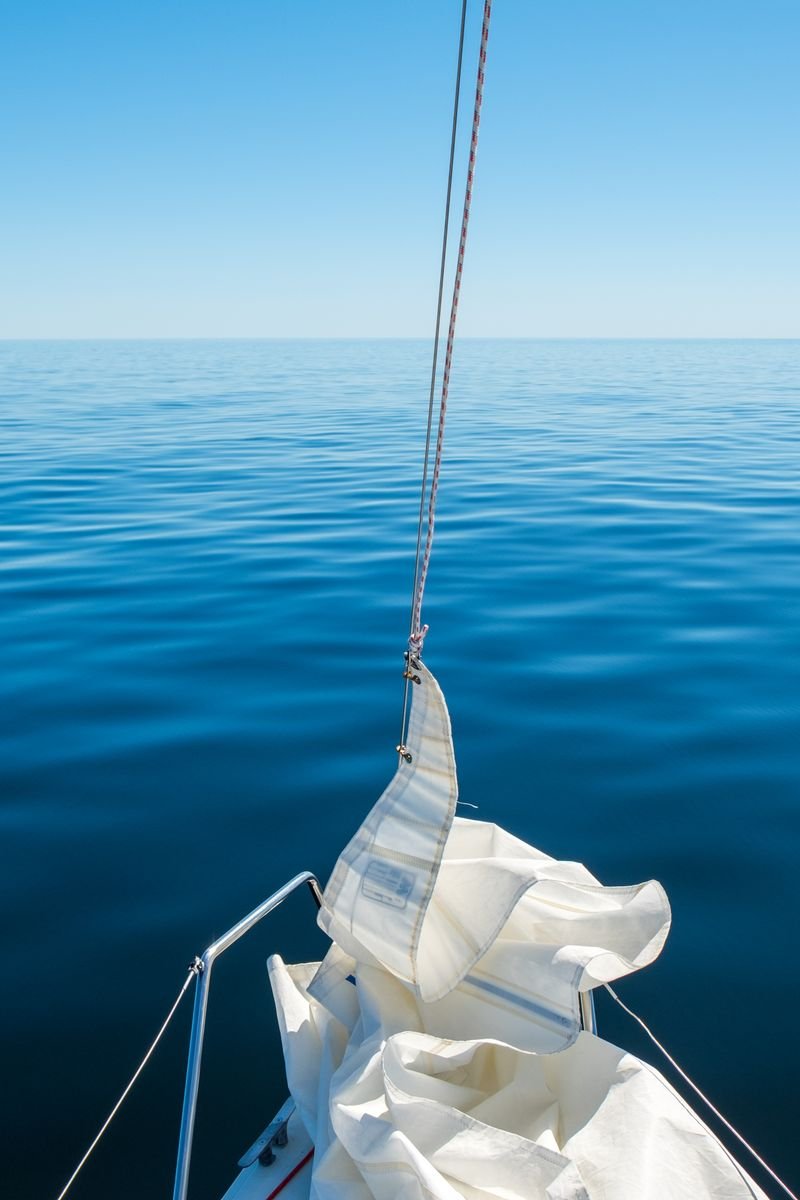 Tranquil scene of a sailboat on a calm, blue ocean under a clear sky, ideal for travel and relaxation themes.